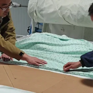 Skilled technicians precisely positioning printed muslin fabric on automated cutting table. Professional spreading ensures grain alignment and cutting accuracy. OEM/ODM manufacturing from professional Chinese B2B baby textile factory.