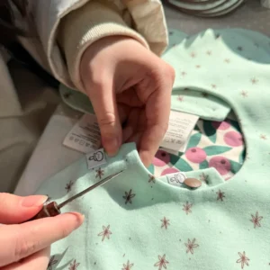 Snap Fastening Process preparation involves precise awl positioning and hole marking ensuring perfect snap alignment. Manual positioning technique optimizes label and fabric coordination. Professional OEM/ODM manufacturing from Chinese B2B baby textile factory.