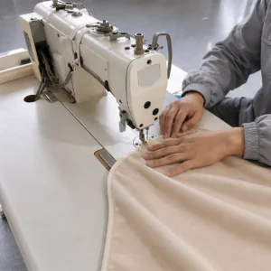 Our skilled technician executes precise perimeter edge binding across a curved cotton fabric layout to create rounded, supple corners. Our baby textile factory in China avoids rigid mechanical feeds for corner processing, ensuring the borders remain soft, flexible, and burr-free.