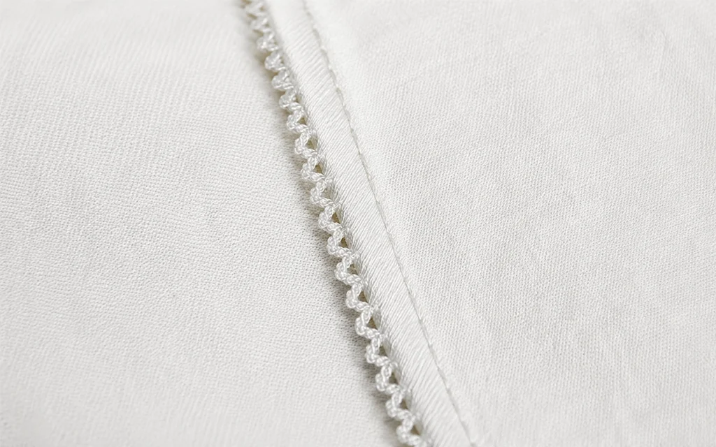 Our custom cotton baby blanket uses a clean, neat white merrow edge with wave-shaped stitching, produced by our Hangzhou, China OEM/ODM baby textile factory with 40+ years of manufacturing experience.