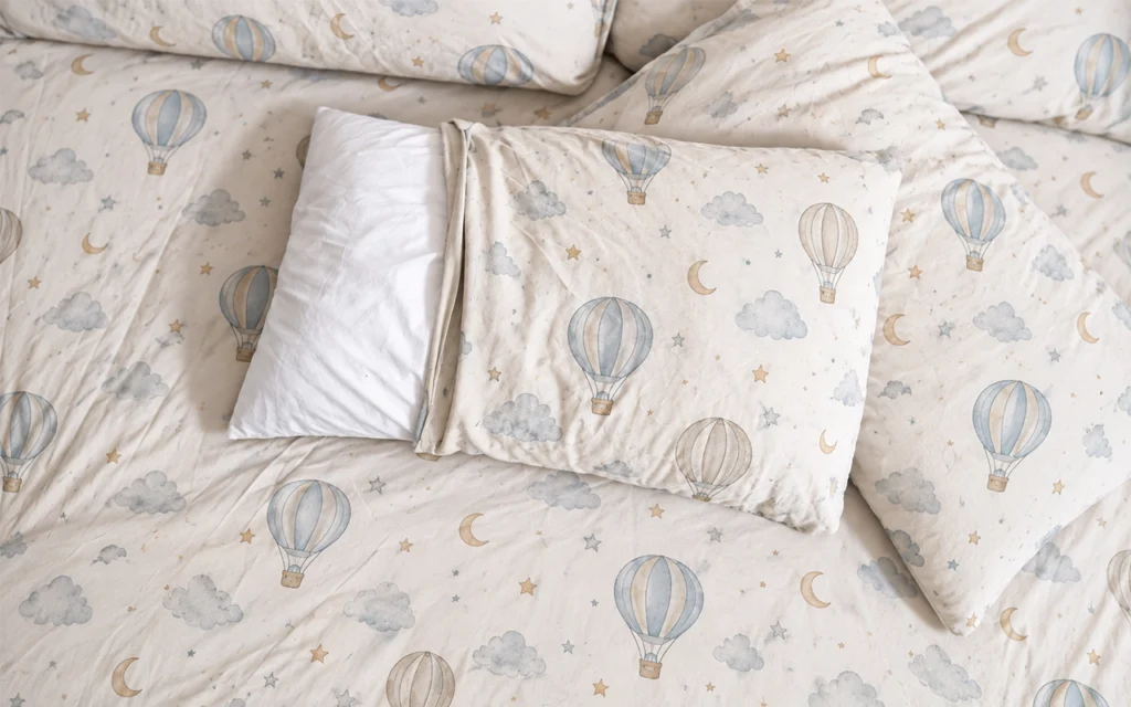 Our overhead bedding scene pairs a white pillow inner with a printed hot-air balloon pillowcase. The cover opening demonstrates how coordinated dimensions affect pillowcase fit and product appearance.